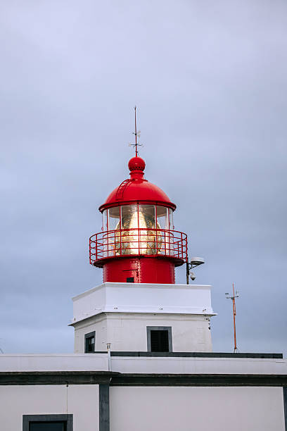 istock Red lighthouse with a glass lantern, standing tall against a cloudy sky 2247989102