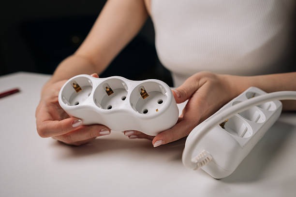 istock Female professional examining white electrical socket sitting at white desk. Woman holding white triple electrical socket in hands. Concept of electrical installation 2247992674