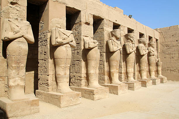 Row of ancient Egyptian pharaoh statues against hieroglyphic temple wall at Karnak in Luxor, Egypt, symbol of history, culture, archaeology and travel.