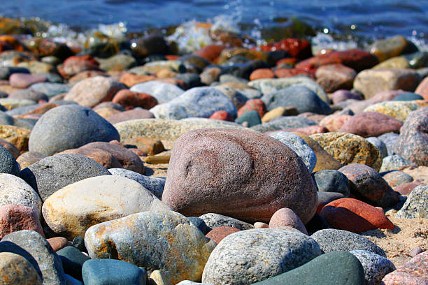 Colorful smooth pebbles on Baltic Sea beach in Poland with blue water in background, natural stone texture and coastal nature concept, horizontal outdoor scene.
