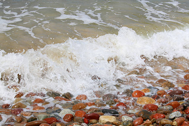 Foamy Baltic Sea wave breaking over colorful wet pebbles on Polish pebble beach, dynamic coastal nature background with copy space.