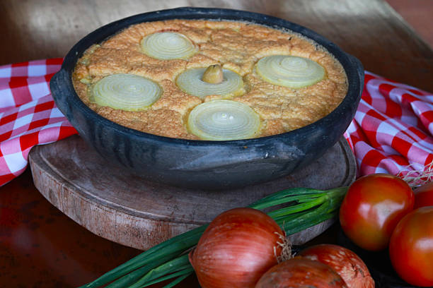 Traditional torta capixaba, a classic Brazilian seafood and vegetable pie typically served during Holy Week in Espírito Santo. Presented in a rustic clay pan, the dish features its iconic onion rings on top and a golden, baked texture.