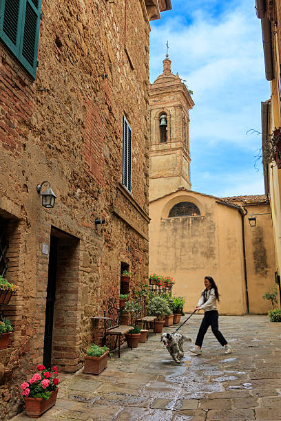 Young woman travels beautiful Tuscan town, Castelmuzio, Italy with her dog