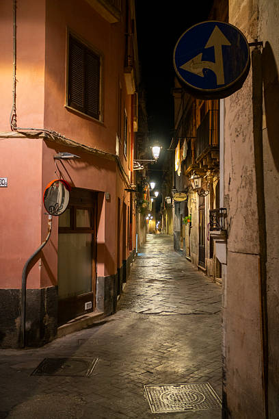 Atmospheric night shot of narrow, illuminated streets in the ancient Ortigia island, Syracuse, Sicily, Italy. The baroque architecture of the old buildings, including a prominent \