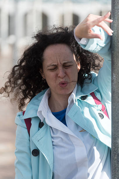 istock A 40-year-old woman in a light blue jacket is leaning against a lamppost, gesturing with her eyes closed and not smiling. 2248004912