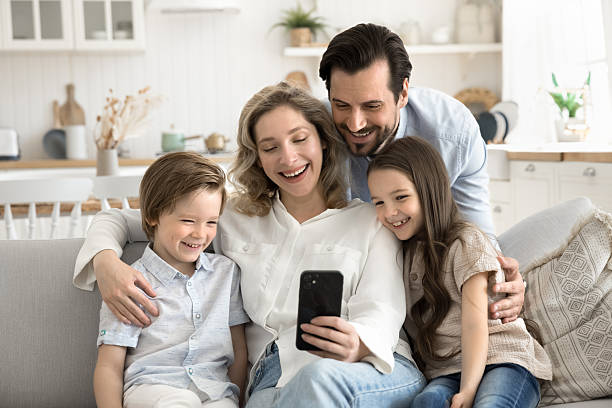 istock Smiling husband hug wife little children on sofa using smartphone 2248019764