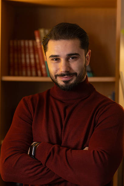 istock Confident man in turtleneck smiling, standing in front of a bookshelf 2248022122