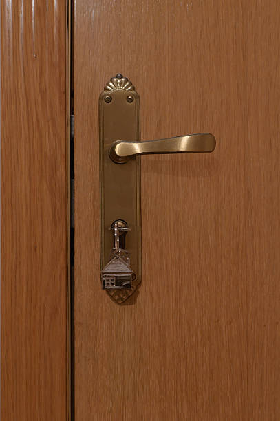 istock Key with a house-shaped keychain hanging in a door lock, symbolizing home ownership, security, access, and real estate concepts against a neutral wooden door 2248022261