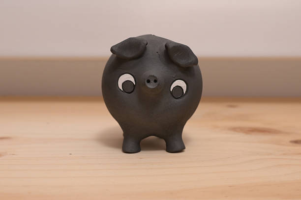 Black ceramic piggy bank on light wood surface, minimalist studio still life symbolizing saving, investment, budgeting, financial planning, wealth accumulation and future security