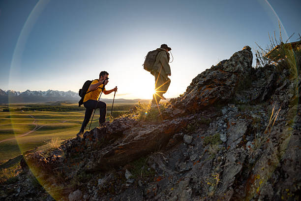 Two young hikers walks uphill at sunset mountain