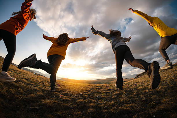 Group of four happy young friends are having fun and runs together at sunset in mountains area
