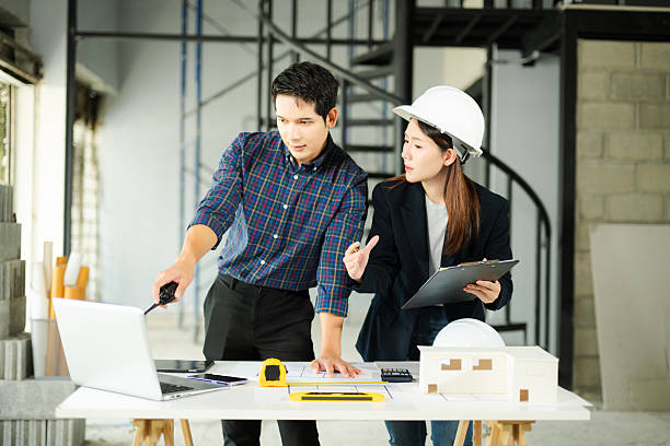 istock Two young Asian architects discussing building plans with laptop, scale model, and hardhat at construction site. Concept of teamwork 2248033495