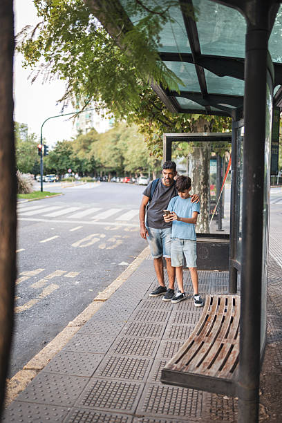 istock Father and son waiting at a bus stop with a smartphone 2248038898