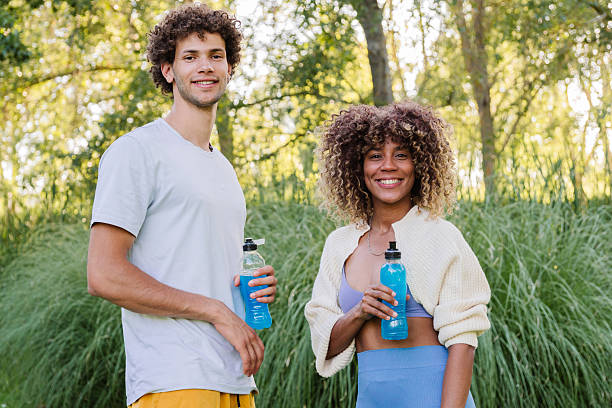 Diverse friends exercising outdoors holding blue sports drinks, smiling at camera after workout, promoting healthy lifestyle, fitness, and active living together