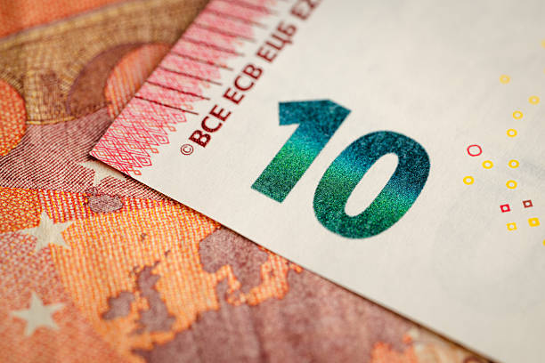 A closeup view of a ten-euro banknote showing the bold green-blue “10” numeral against a clean white area, contrasted with the warm red map and star patterns beneath. Fine security dots and detailed printing textures highlight the precision of euro currency design. The composition emphasizes color contrast and intricate linework.