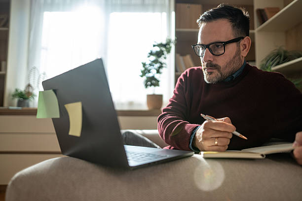istock Man working on laptop and taking notes at home 2248050318