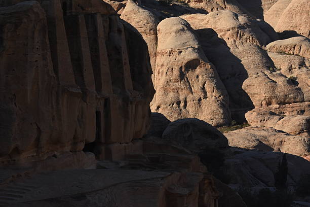 Visitors marvel at the intricate carvings of ancient tombs in Petra, Jordan, surrounded by stunning rock formations and deep canyons during midday.