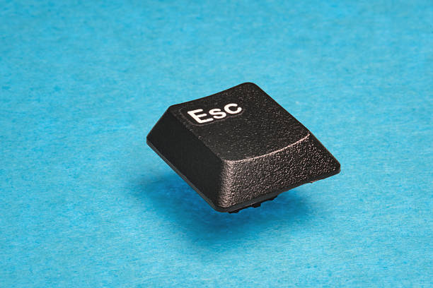 Macro studio shot focuses on a black plastic Esc keycap floating diagonally over a vibrant textured cyan background. Symbolizing stopping or quitting. Great for tech advertising.