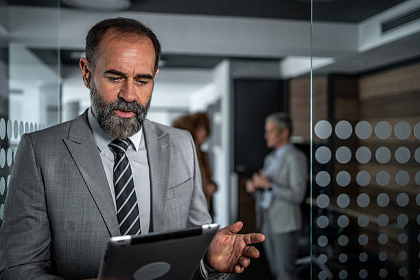 istock Mature adult businessman using tablet discussing project in office 2248059644