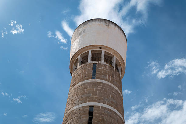 A historic cylindrical water tower, clad in stone and cement, stands out against a blue sky and scattered clouds in Portugal
