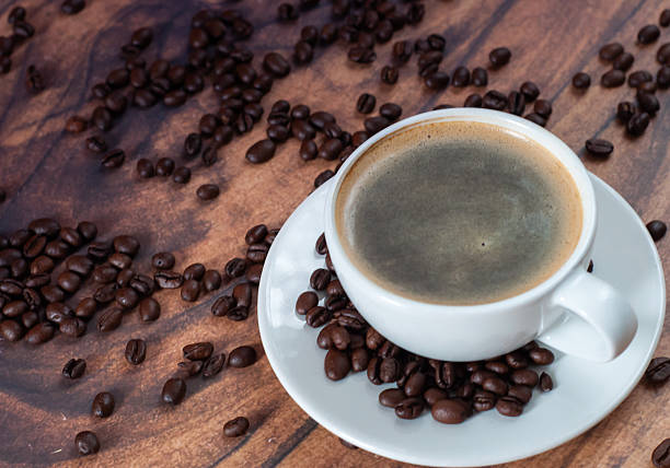 A white coffee cup with black coffee stands on a wooden table.