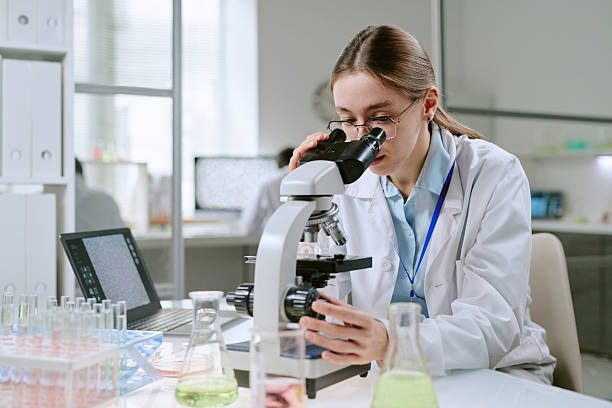 istock Young Adult Caucasian Woman Observing Specimen Slide through Laboratory Microscope 2248065568