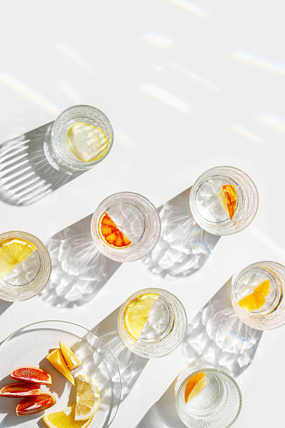 istock Crystal glasses with citrus slices in water on white background with rainbow reflections at sunlight, modern, minimal composition with glass cups filled with water and citrus fruit, as lemon orange 2248070221