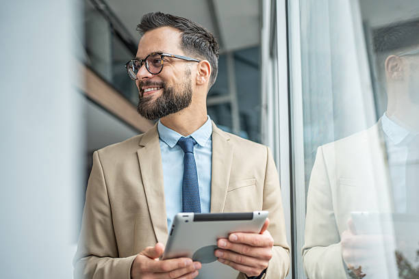 istock Happy businessman holding tablet looking out window 2248072516