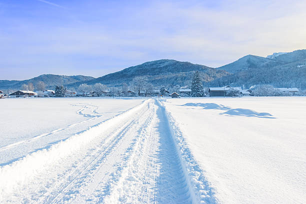 Snow covered road in the Bavarian Alps, the road leads over a railway crossing to a small village near Benediktbeuern in Upper Bavaria, Germany.
