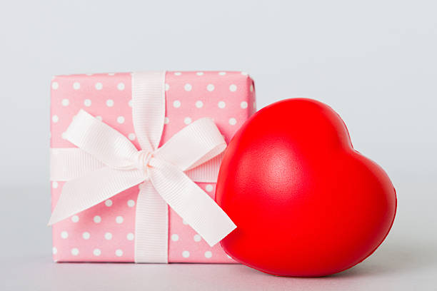 gift box with red bow and red heart on colored background. Perspective view. Flat lay.
