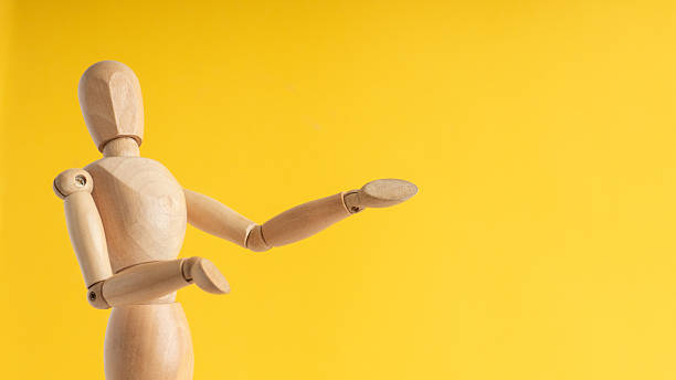 istock Wooden mannequin presenting with open arm on yellow backdrop 2248078854