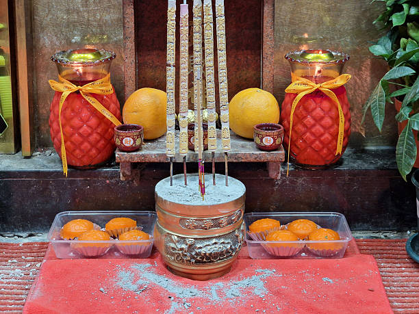 Hong Kong,  China -  2024-05-09: Incense sticks, candles, cakes and fruit offerings arranged at a small street shrine in Hong Kong, China, for luck and protection.