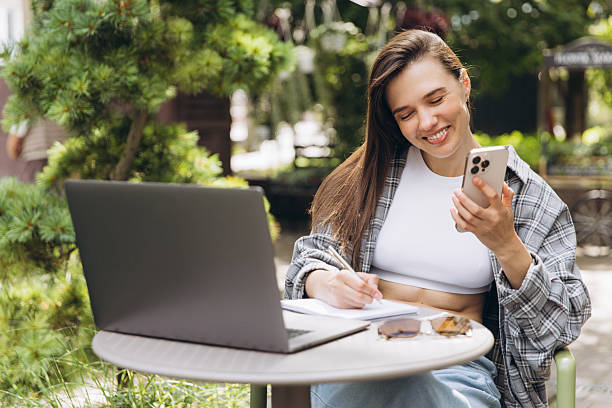 istock Woman working remotely outdoors using laptop and phone 2248084487