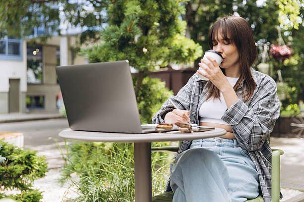 istock Young woman working remotely outdoors drinking coffee 2248084685