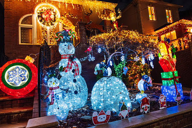 Colorful holiday lights illuminate a brick house front yard featuring lit snowmen, giant gifts, and festive decorations. A joyful Christmas scene perfect for family, celebration, and seasonal home decor imagery.Brooklyn, NYC, USA