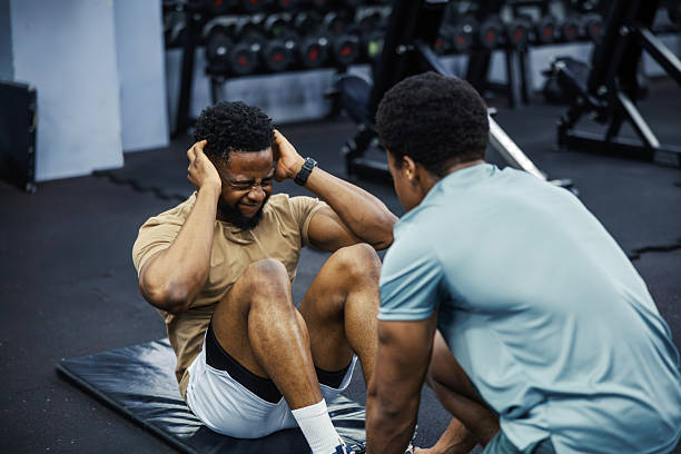 istock Man doing sit-ups with personal trainer in gym 2248093441