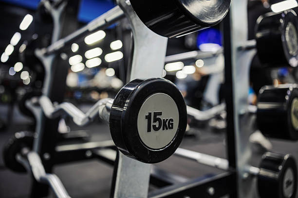 Barbell weights resting on a rack inside a modern fitness gym, highlighting a 15kg plate ready for strength training