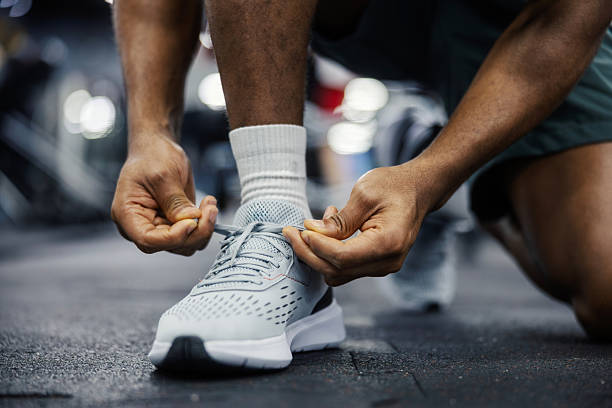 Man preparing for fitness training, tying running shoe laces on a gym floor, focusing on an active lifestyle