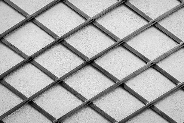 Monochrome lattice grid spans a textured wall, creating an abstract, geometric backdrop ideal for design, architecture, or mood imagery emphasizing structure, repetition, and contrast.