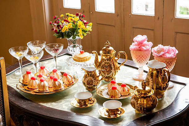 An elegantly set table with porcelain tableware, all in a sophisticated vintage style reminiscent of the 18th century. The composition is warm, with a predominance of gold, pink, and floral details. Natural, diffused light.