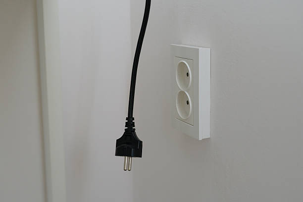 istock Black power cord hangs from a wall socket in a clean, minimalist room, ready for use. Natural light enhances the simple design of the space 2248097645