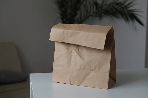 istock A brown paper lunch bag sits on a white table. The soft sunlight highlights its texture, creating a calm atmosphere in a simple setting 2248097660