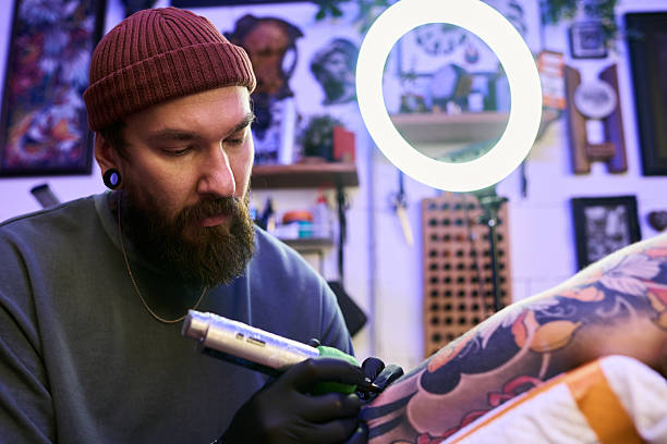 istock Bearded Young Man Concentrating While Tattooing Client Leg 2248101364