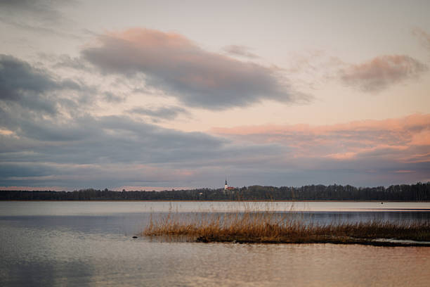 Tranquil lake landscape at sunset, showcasing calm waters and pastel clouds, with tall grass along the shoreline, evoking a peaceful outdoor atmosphere