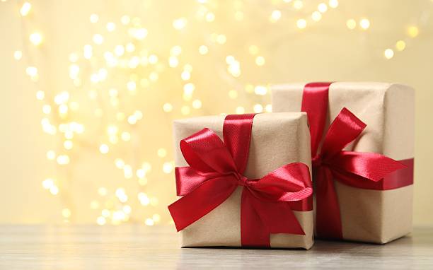 istock Wrapped gifts with red ribbons on table with bright bokeh behind 2248102545