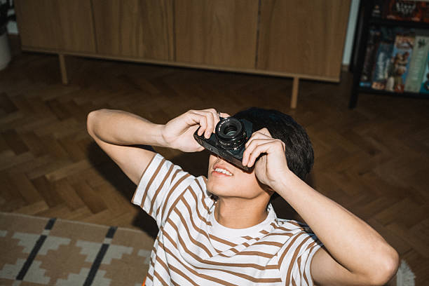Medium shot of a young man with dark hair operating a vintage film camera, wearing a striped shirt.