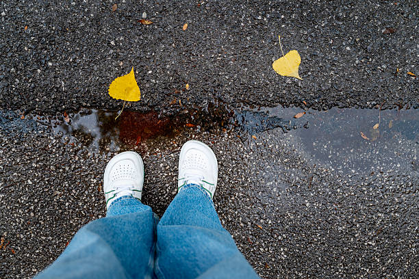 White shoes with blue jeans on wet asphalt with autumn leaves