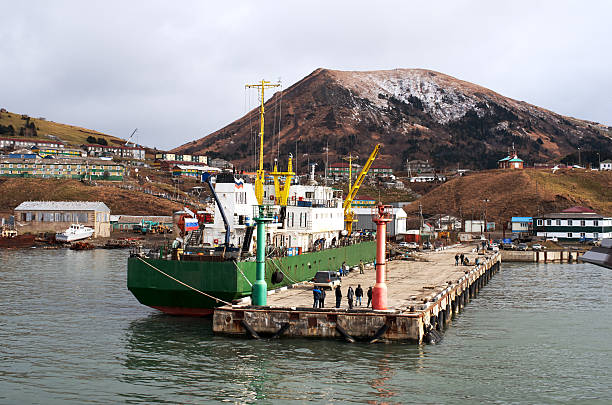 Pier and moored ship in Malokurilskoye Bay. View of Malokurilskoye village. Southern Kuril islands. Shikotan island - one of the bigger islands of the Kuril Islands. Unrecognize person