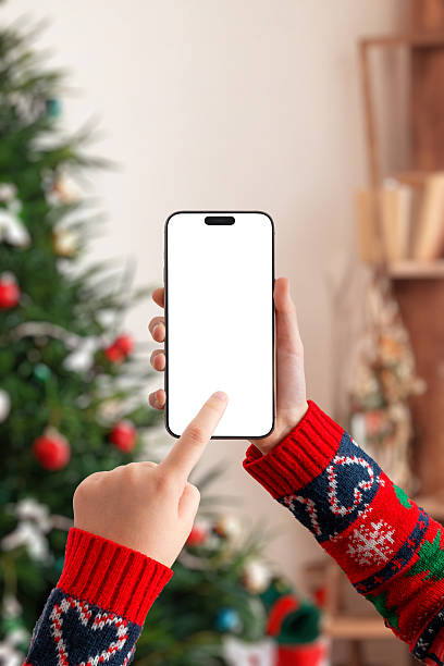 istock Hand holding smartphone horizontally with blank screen near Christmas tree, perfect for video mockups, streaming apps, holiday marketing and festive UI presentations 2248109972