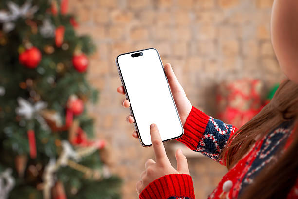 istock Hand holding smartphone with blank screen in cozy Christmas setting, ideal for app mockups, holiday promotions, mobile UI presentations and festive marketing visuals 2248109973